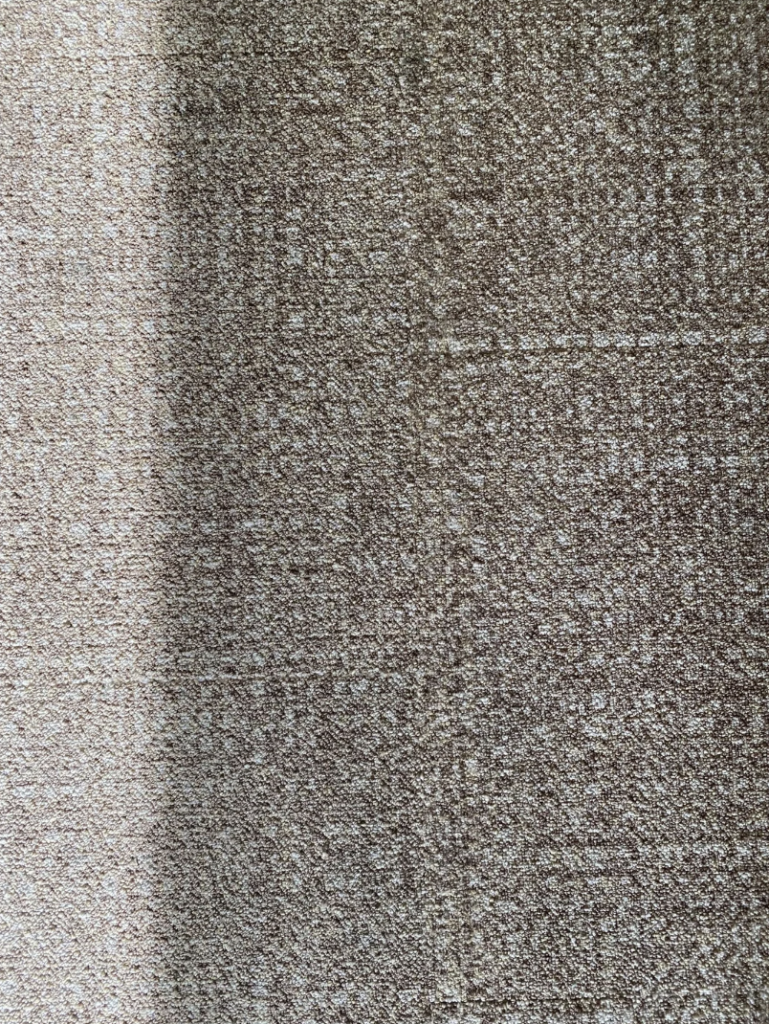 A close-up view of a textured, beige and brown patterned fabric. The fabric has a combination of light and dark shades, creating a subtle, visually appealing design.