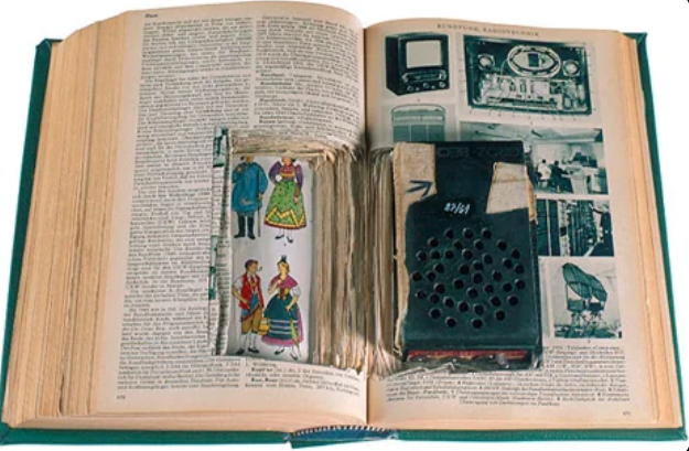 An open book with the pages carved out to accommodate a small dollhouse scene and a vintage miniature television model. The left side shows illustrations of people in traditional clothing, while the right side depicts various old-fashioned electronic devices.