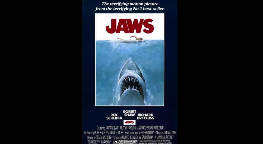 An iconic movie poster for "Jaws" features the title in bold red letters at the top against a blue ocean backdrop. Below, a swimmer is depicted on the surface while a great white shark emerges from below, mouth open wide. Cast names are listed near the bottom.