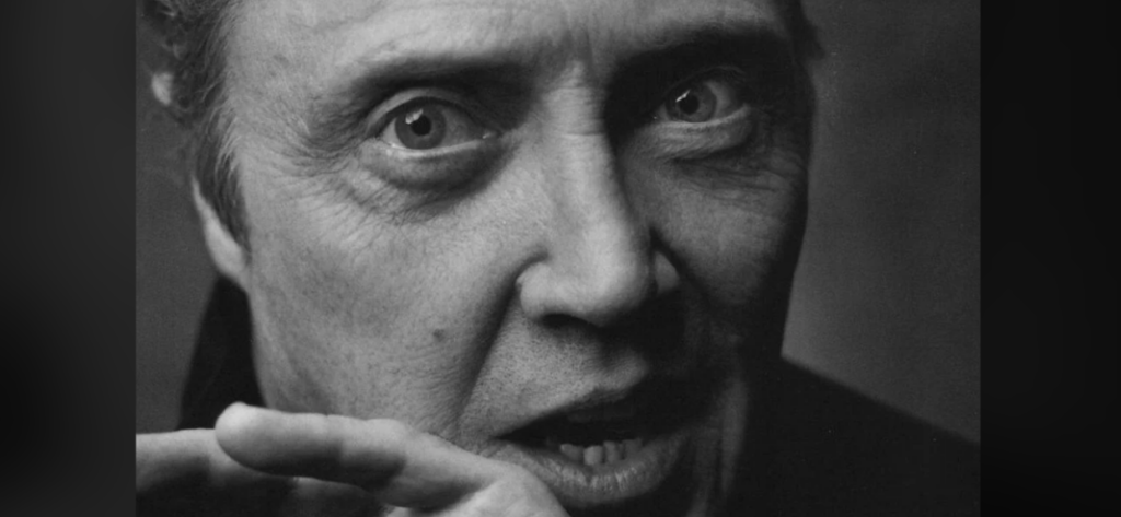 Black and white close-up photo of an older man with intense eyes and expressive facial features. He appears to be in mid-conversation, with his hand partially raised as if emphasizing a point. The image captures detailed textures of his skin and hair.