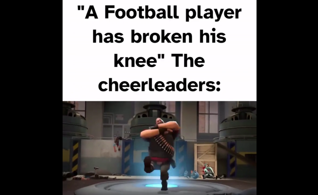 Text at the top reads, "'A Football player has broken his knee,' the cheerleaders:". Below is an animated scene depicting a character from the game Team Fortress 2 doing a victory dance in a factory setting, suggesting cheerleaders celebrating despite the player's injury.