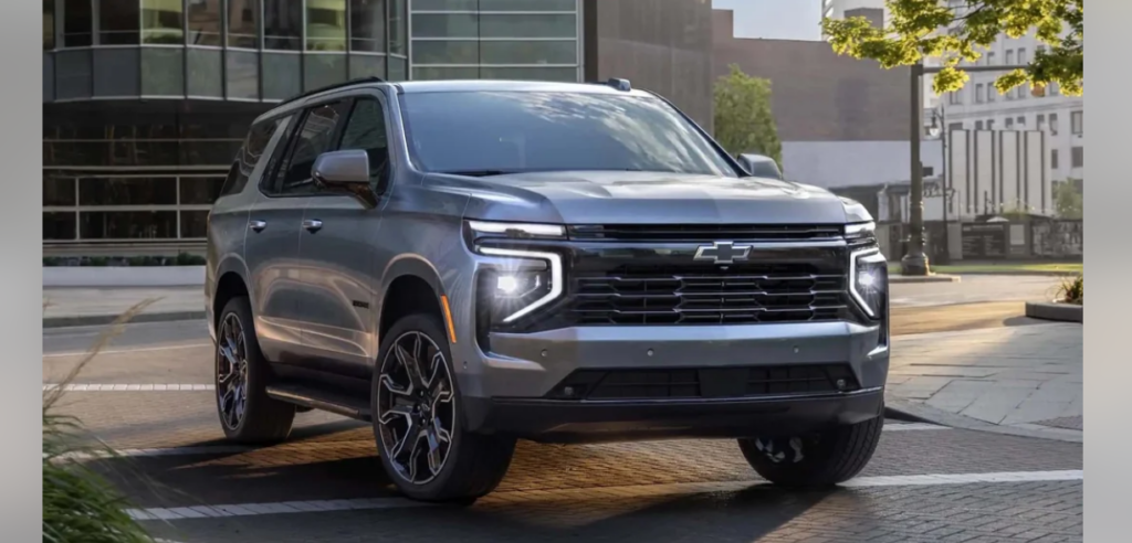 A sleek, silver Chevrolet SUV is parked on an urban street with modern buildings in the background. The vehicle features distinctive LED headlights, a prominent grille with the Chevrolet logo, and stylish alloy wheels. Sunlight highlights the vehicle's clean lines.