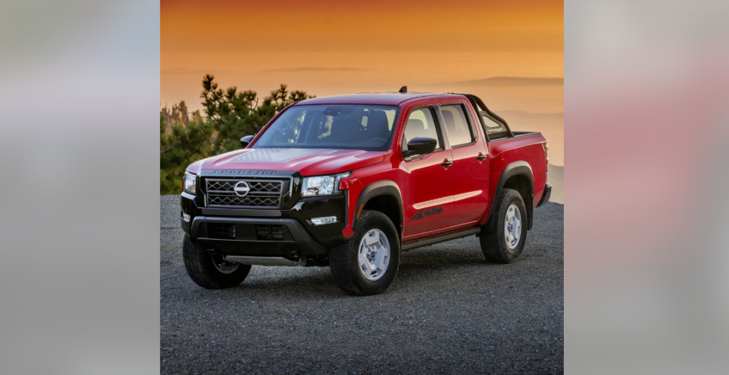 A red Nissan Frontier pickup truck is parked on a pavement area. The backdrop features a captivating orange and yellow sunset with silhouettes of trees and hills, giving the scene an adventurous and rugged outdoor ambiance.