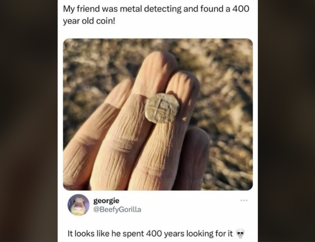 A person holding an old, weathered coin in their fingers. The top caption reads, "My friend was metal detecting and found a 400 year old coin!" Below, a tweet from @BeefyGorilla says, "It looks like he spent 400 years looking for it" followed by a skull emoji.