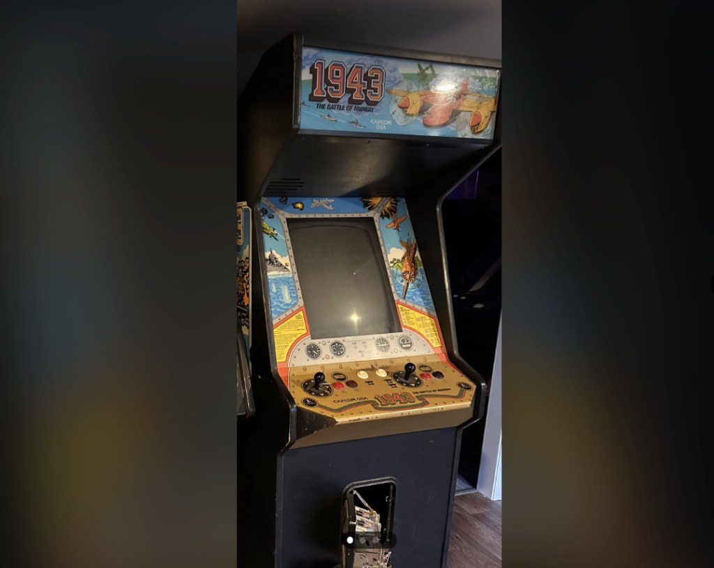 An arcade machine for the game "1943: The Battle of Midway" featuring colorful game artwork around the screen and joystick controls. The cabinet's lower front has a coin slot mechanism, and the game title is prominently displayed above the screen.