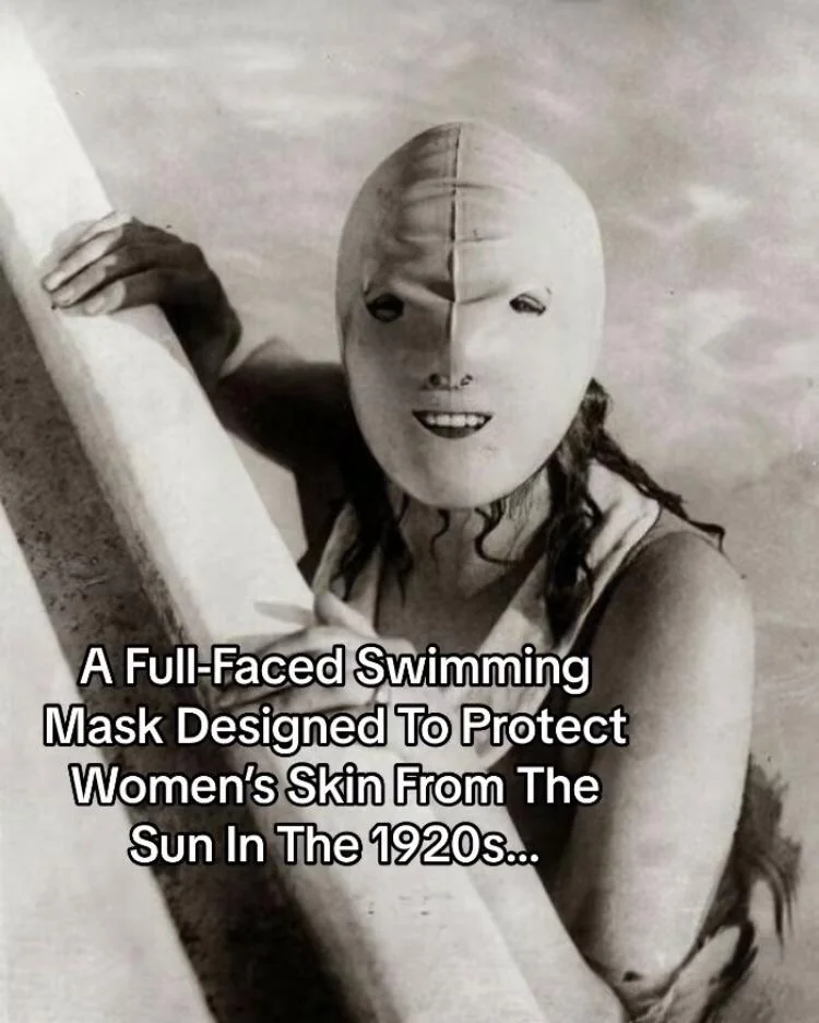 A vintage black-and-white photo shows a person wearing a full-faced swimming mask designed to protect women’s skin from the sun in the 1920s. The mask covers the entire face with only small openings for the eyes, nose, and mouth.