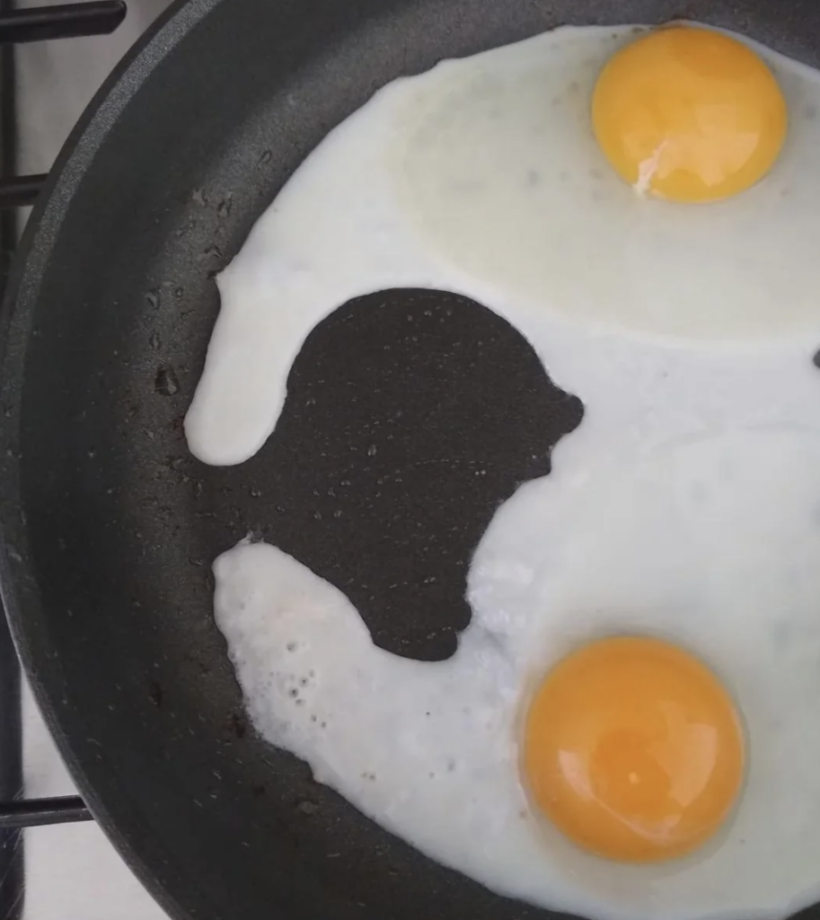 A frying pan with two sunny-side-up eggs, where the egg whites have formed an unusual, fish-like shape in the middle of the pan, leaving a black patch of the pan's surface exposed. The bright yellow yolks are at opposite ends of the pan.