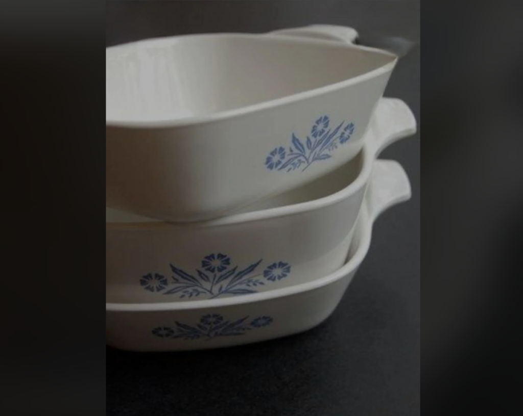 A stack of three white ceramic casserole dishes with blue floral patterns on the side, positioned against a dark background. The dishes have handles and are nested inside one another.