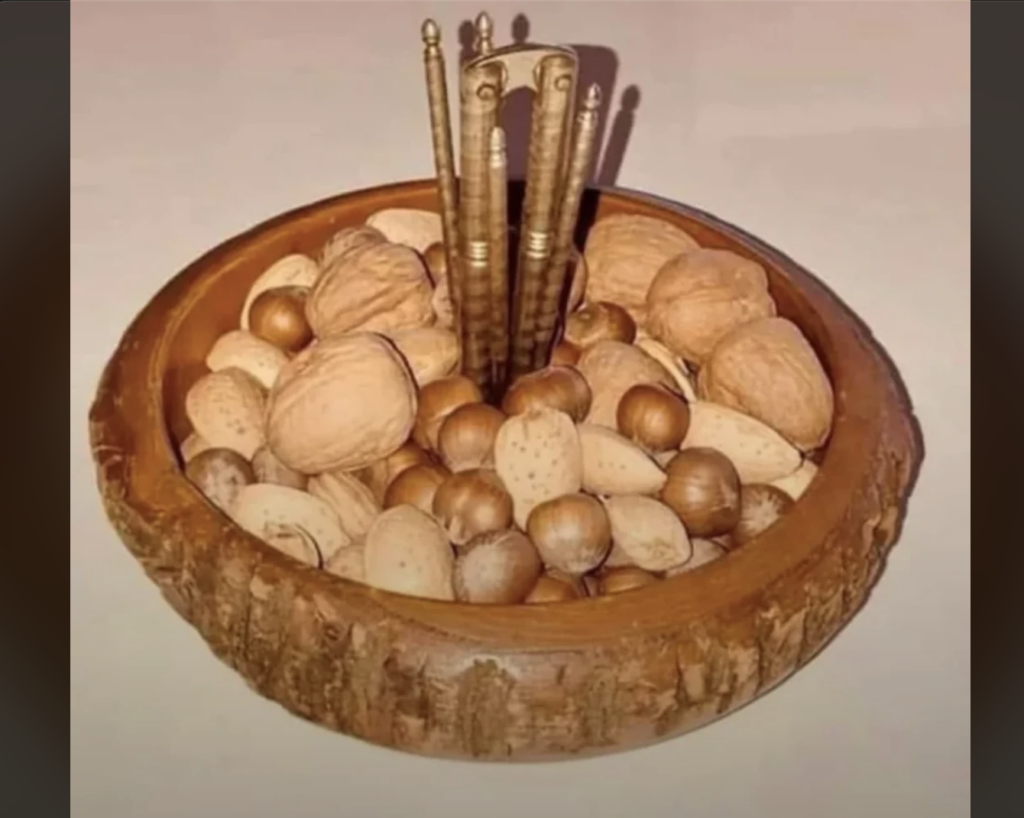 A wooden bowl filled with various types of nuts, including almonds, hazelnuts, and walnuts, is featured. In the center of the bowl, there are five intricately designed metallic nutcrackers standing upright.