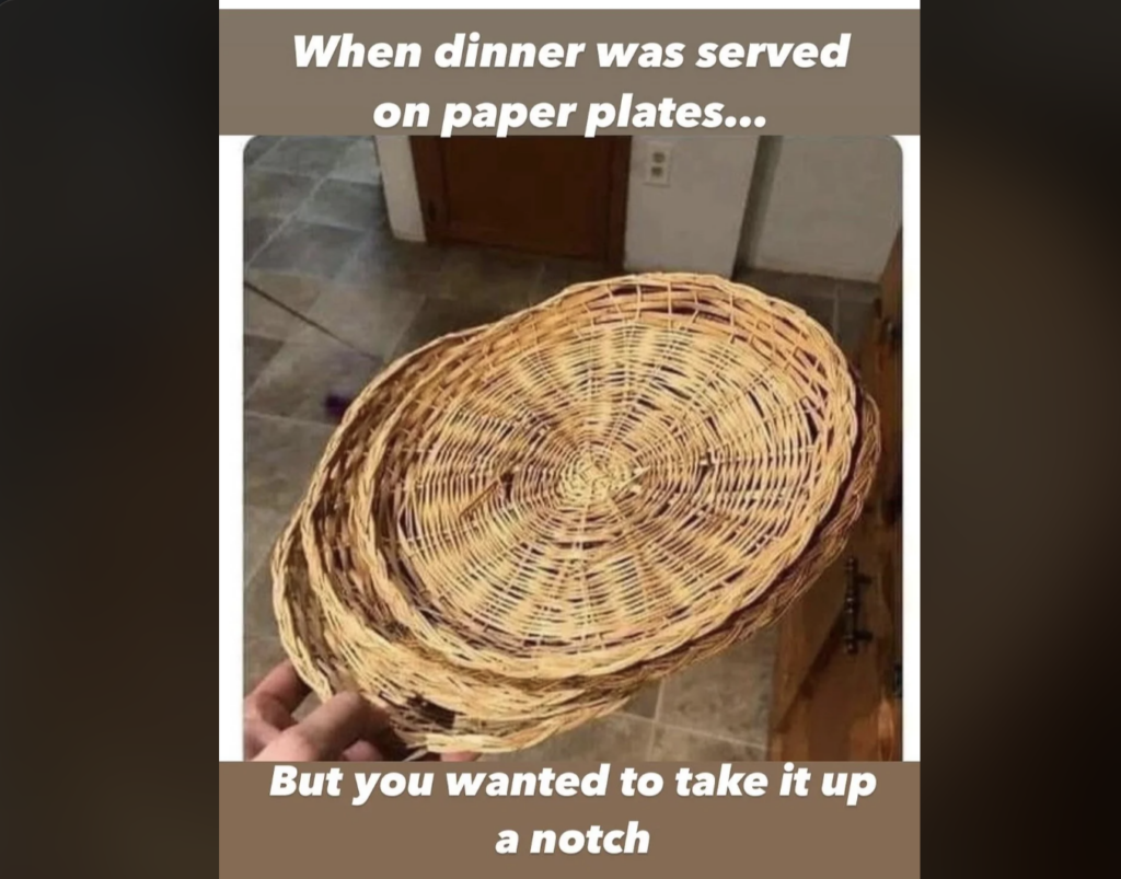 A hand holds a flat, woven wicker tray resembling a paper plate. The image has text above and below. Top text: "When dinner was served on paper plates..." Bottom text: "But you wanted to take it up a notch." The background shows a tiled floor and kitchen cabinets.