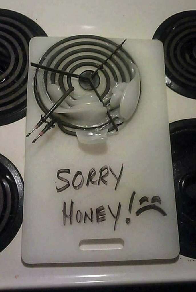 A white cutting board with broken ceramic pieces and a wire coil. The board has "SORRY HONEY!" written on it with a sad face. The scene is set on a stovetop with visible burners.