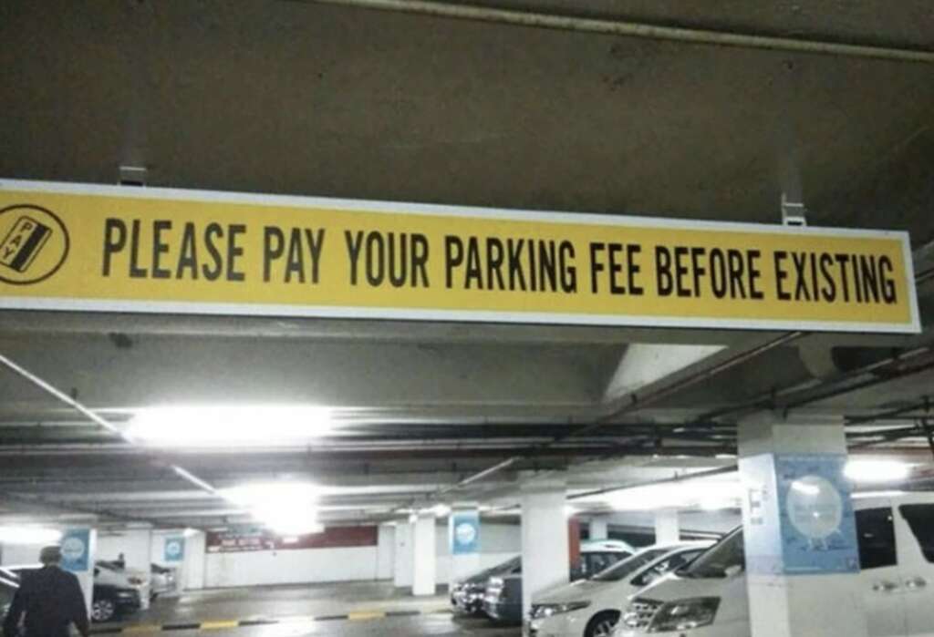 A sign in a parking garage reads "PLEASE PAY YOUR PARKING FEE BEFORE EXISTING" with a humorous typo. Several cars are parked in the background under dim lighting.