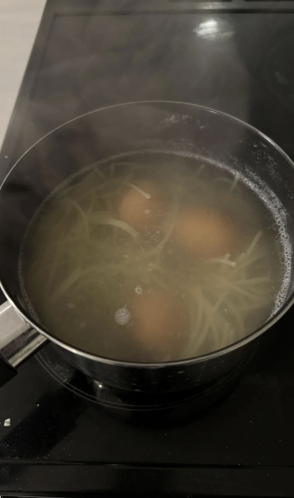 A mildly infuriating scene unfolds as a pot on the stove contains boiling water with three eggs and some spaghetti, while steam rises mockingly from the chaotic mix.