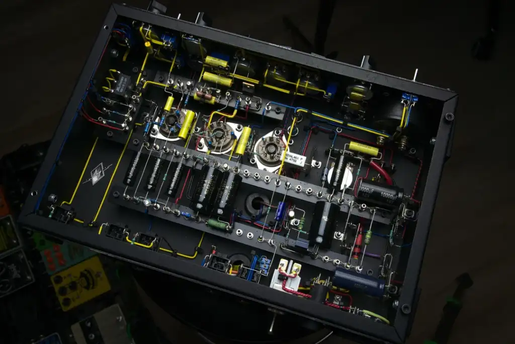 Overhead view of the internal circuitry of an amplifier. The metal chassis displays various electronic components such as capacitors, resistors, and wires. The setup is neatly organized, showcasing a complex and intricate design.