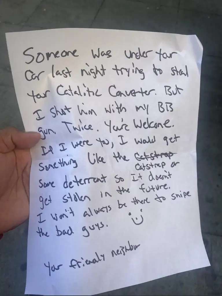 A handwritten note on white paper, held by a hand, describes a neighbor stopping an attempted theft of a catalytic converter with a BB gun. The note suggests getting a deterrent for future protection.