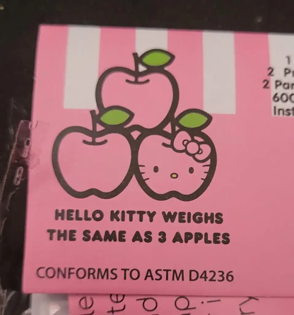 A pink label featuring Hello Kitty and three apples. The text reads, "Hello Kitty weighs the same as 3 apples." The background has pink and white stripes.