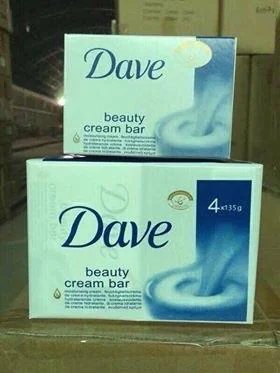 Two boxes of "Dave" beauty cream bar soap are stacked. The packaging is white and blue with a swirl design. Each box contains 4 bars weighing 135g each. The boxes are displayed in a storage or warehouse setting.