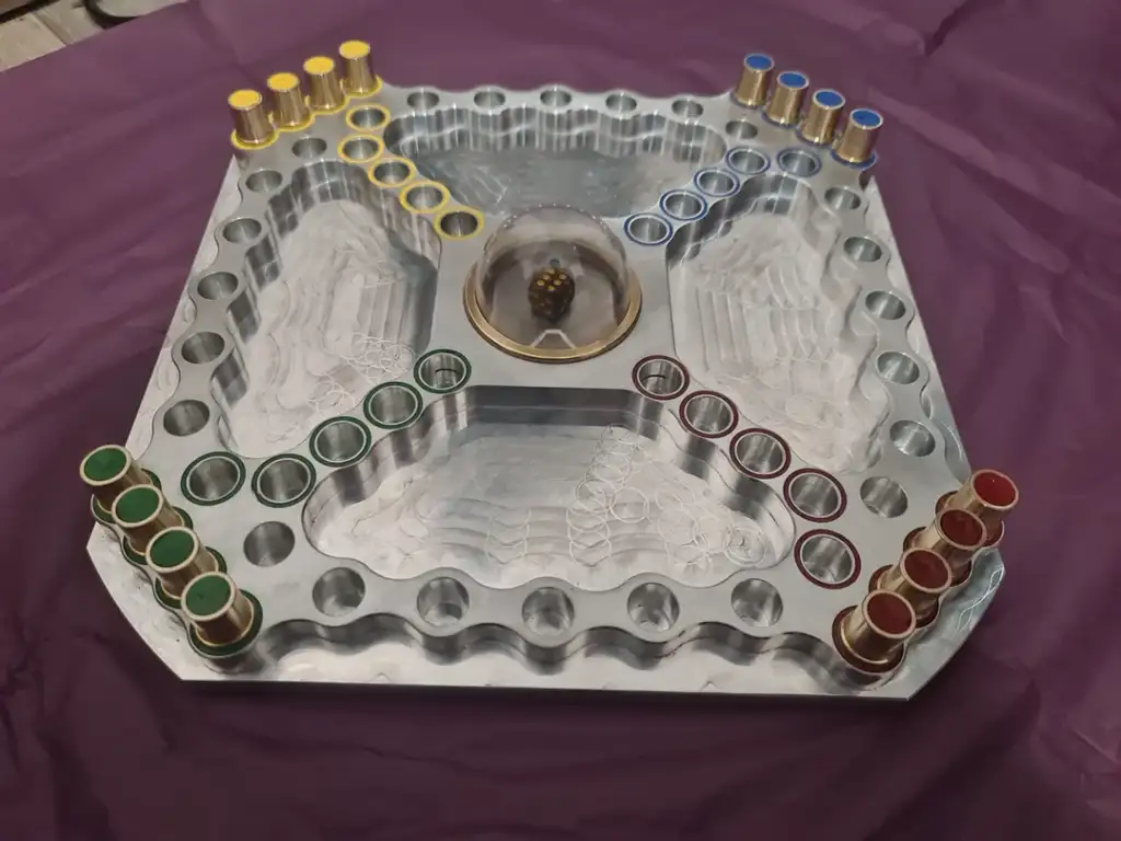 A metal board game with colored pegs in rows. The board has circular slots and a central dome containing dice. The background is a purple surface.