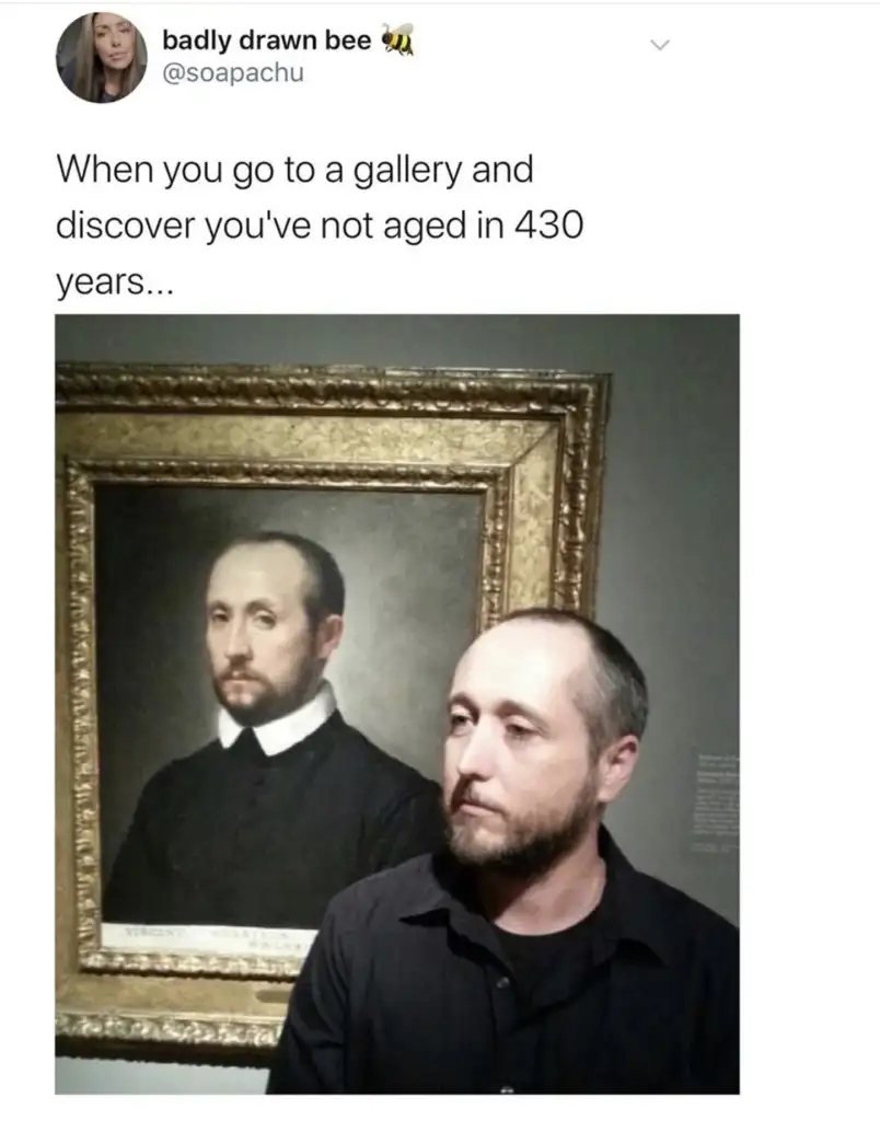 A man stands next to a painting in a gallery. The painting depicts a historical figure that closely resembles him, both having similar hairstyles and beards. The caption humorously suggests the man hasn't aged in 430 years.