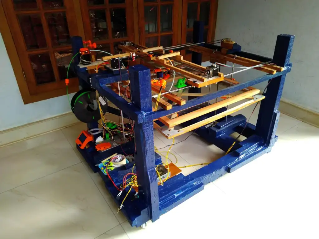 A homemade 3D printer with blue and wooden structural components is set up in a room with a tile floor and wooden windows. Various wires and electronic parts are visible on the printer.