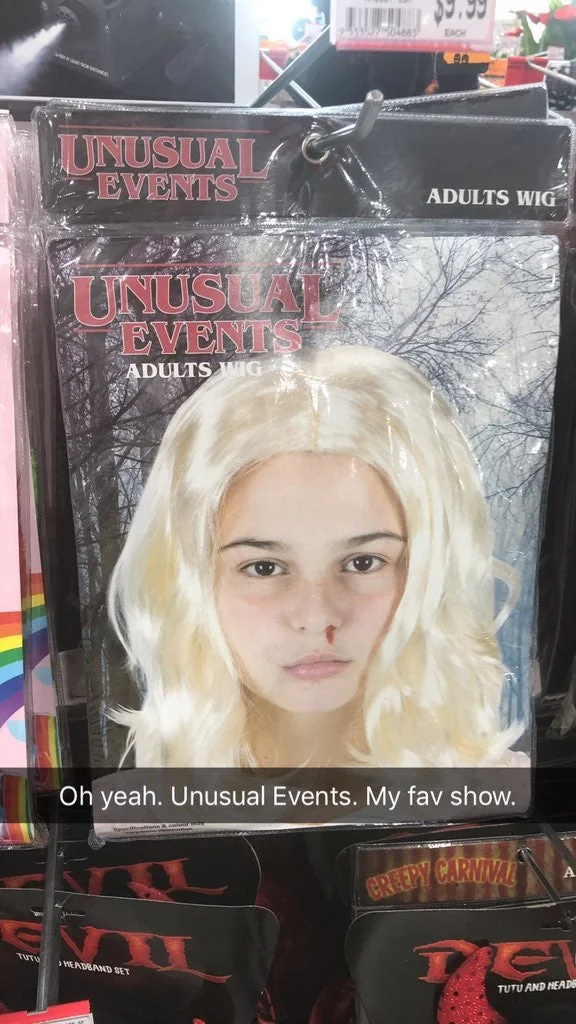 A package labeled "Unusual Events Adults Wig" displays a person wearing a platinum blonde wig against a background of leafless trees. A Snapchat caption reads, "Oh yeah. Unusual Events. My fav show.