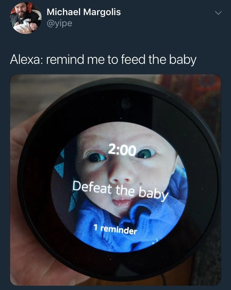 A hand holds a device displaying a reminder set for 2:00 with the text "Defeat the baby." A baby's face is seen on the screen. The caption above reads "Alexa: remind me to feed the baby.