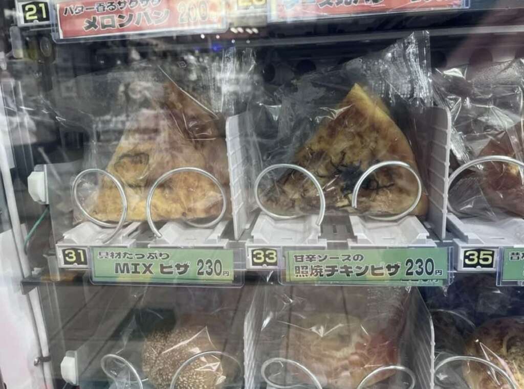 A vending machine displays food items in plastic wrap. Two items labeled "MIX Pizza" and "Chicken Pizza," priced at 230 yen each, are visible. Other items are partially visible inside the machine.