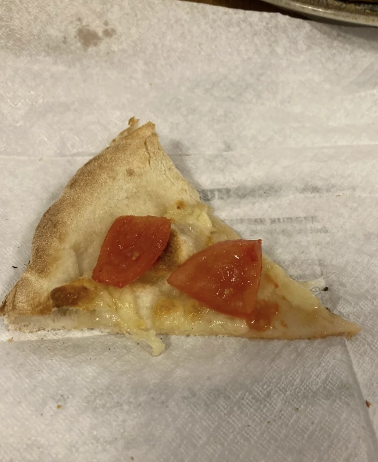 A slice of cheese pizza with two pieces of tomato on top, placed on a white napkin.