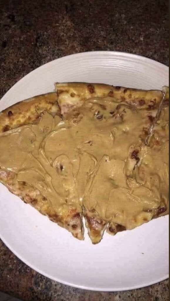 Three slices of pizza on a white plate, topped with a thick layer of light brown peanut butter, resting on a granite countertop.