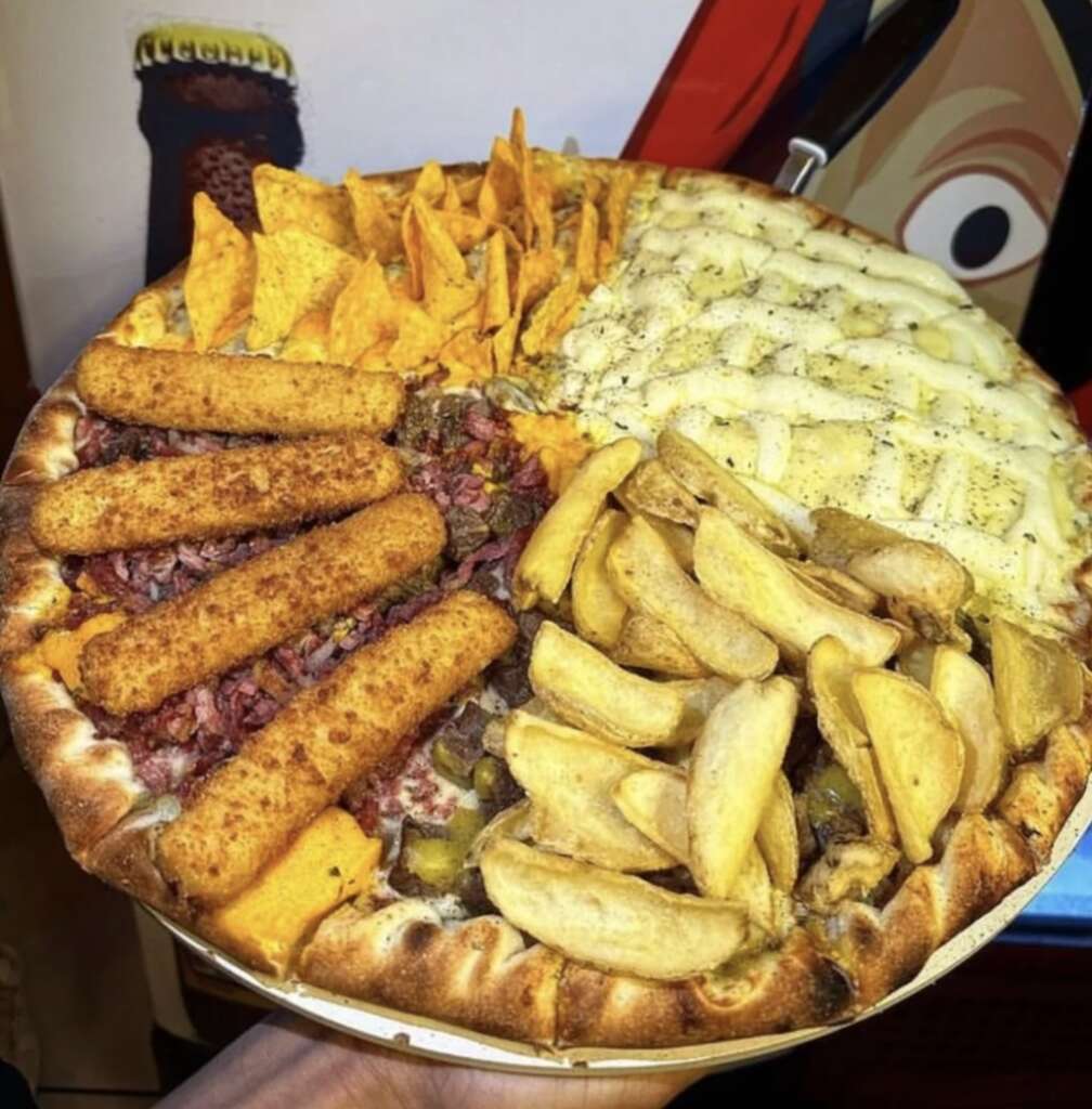 A pizza is divided into sections with different toppings: triangular chips, cheese, potato wedges, mozzarella, and breaded sticks. A colorful background with abstract designs is partially visible behind the pizza.