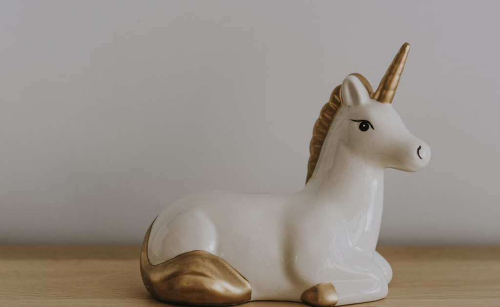 A ceramic unicorn figurine with a gold horn, mane, tail, and hooves is laying on a wooden surface against a plain background.