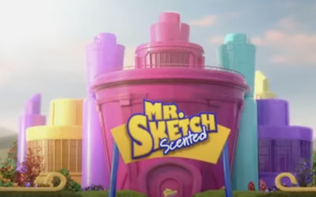 A colorful factory with purple, pink, yellow, and teal buildings, featuring a large pink structure in the center. The building is labeled "Mr. Sketch Scented" in bold yellow and blue text. Bright greenery surrounds the factory.