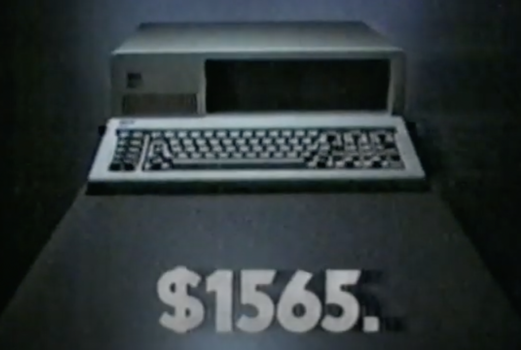 A vintage computer with a built-in keyboard is displayed on a dark table. The price, "$1565," is prominently shown in the foreground. The computer appears to be from an earlier era, likely the 1980s.