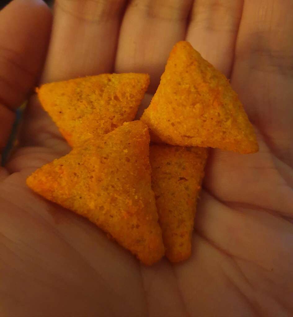 Four Dorito 3ds; triangular, orange corn chips with a textured surface rest on an open palm.