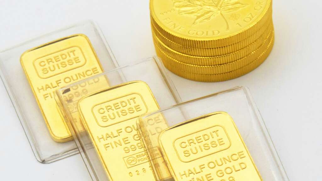 Stacked gold coins and three Credit Suisse gold bars are displayed. The bars are labeled "HALF OUNCE FINE GOLD 999.9". The coins feature a maple leaf design.