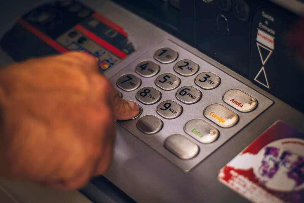 A person’s hand pressing buttons on an ATM keypad. The keypad includes numbers and commands like "Cancel" and "Enter." The hand is selecting the number 8. The surrounding area shows parts of the ATM interface.