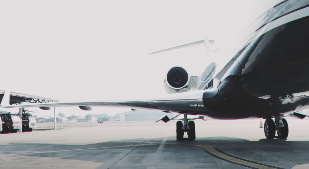 View of a sleek private jet on an airport tarmac, with its engines and wings visible. The background shows part of the hangar and a clear sky.