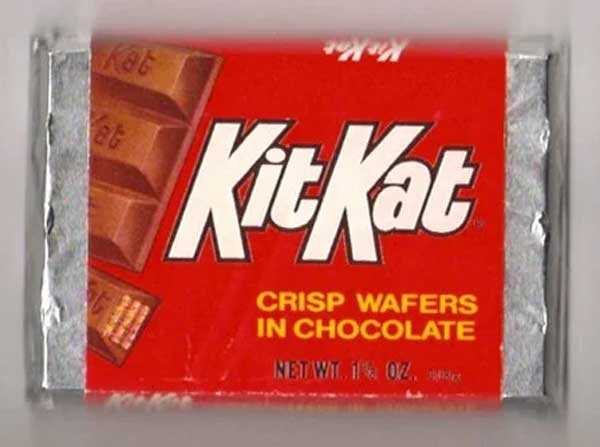 Red Kit Kat wrapper with bold white logo. Features an image of chocolate-covered wafer pieces and text "CRISP WAFERS IN CHOCOLATE." Silver foil edges are visible. Net weight listed as 1½ oz (42g).