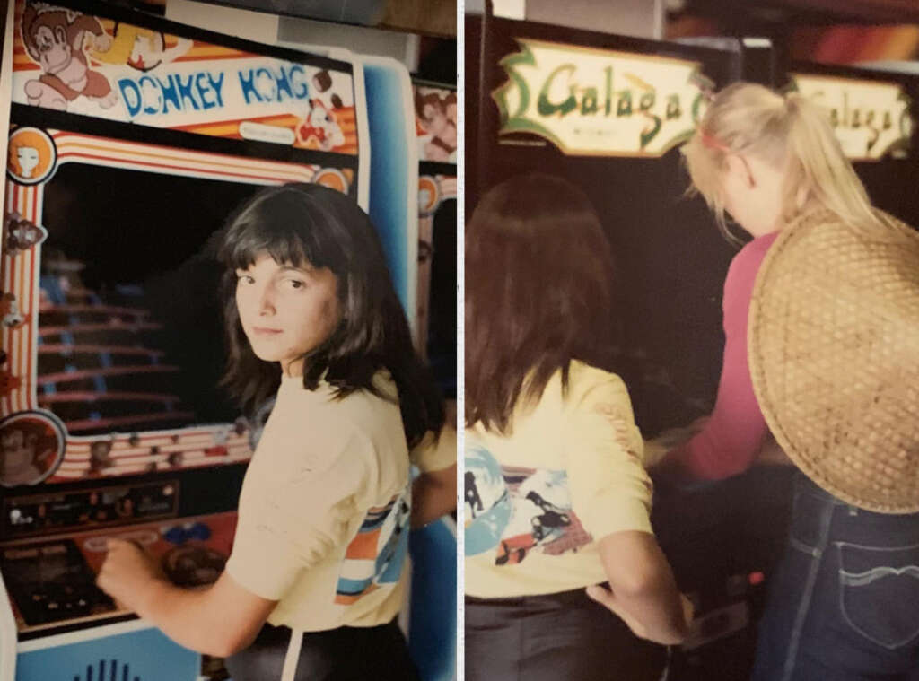 Two young women playing arcade games: one plays Donkey Kong, glancing back over her shoulder, while the other, wearing a straw hat on her back, plays Galaga. Both are focused on their respective games in a retro arcade setting.