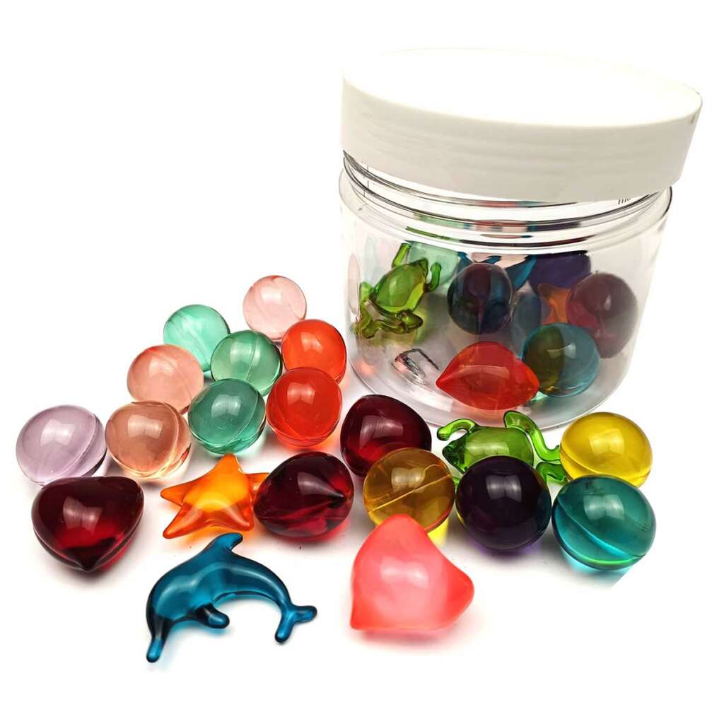 A container with a white lid is surrounded by colorful gel beads and shapes, including stars, a dolphin, and a frog on a white background. The beads are in various colors like pink, green, orange, red, and blue.