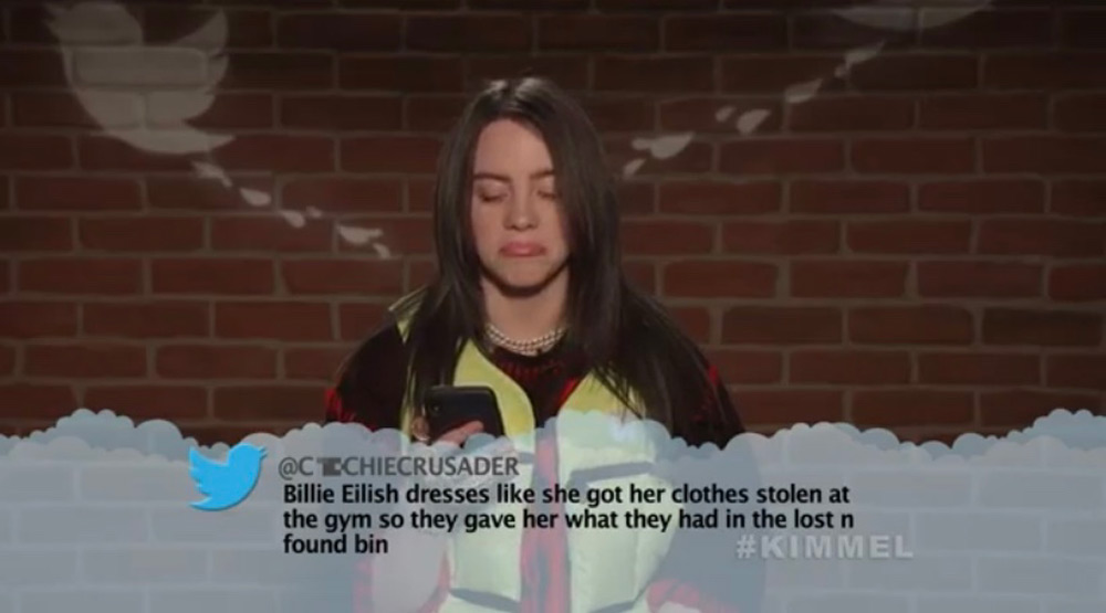 A person with long dark hair looks at a phone, standing against a brick wall background. A humorous tweet appears on screen, joking about how their clothing was found at a gym's lost and found bin. The hashtag #KIMMEL is visible.