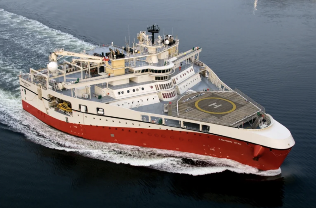 A large red and white maritime vessel named "Ramform Titan" is cruising on the water. The ship features a helipad on its deck and various equipment and structures, including cranes and antennas, suggesting it is equipped for specialized tasks.