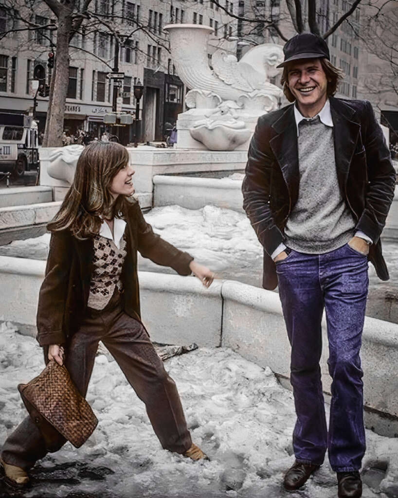 A young girl and a man stand in front of a fountain in a snowy urban setting. The girl wears a patterned vest and brown clothes, holding a bag. The man, in a cap and velvet jacket, smiles with hands in pockets. Both appear joyful.