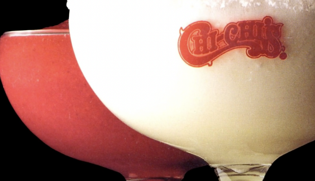 Close-up of two margarita glasses. The left glass contains a red frozen drink, while the right has a white frozen drink with the Chi-Chi's logo on the glass. Both drinks are set against a black background.