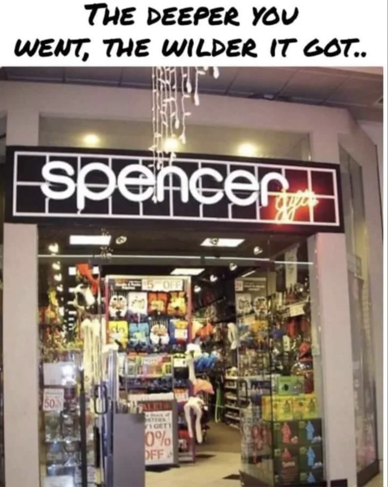 Storefront of Spencer's in a mall, displaying assorted colorful items. The sign above reads "Spencer Gifts" with neon lights. A caption on top says, "The deeper you went, the wilder it got.