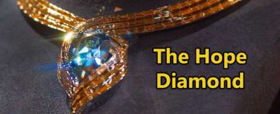 A close-up of the Hope Diamond necklace displayed on a dark surface. The diamond is a deep blue, surrounded by an intricate gold setting. The words "The Hope Diamond" are written in bold yellow text.