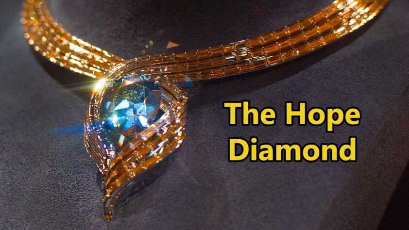 A close-up of the Hope Diamond necklace displayed on a dark surface. The diamond is a deep blue, surrounded by an intricate gold setting. The words "The Hope Diamond" are written in bold yellow text.