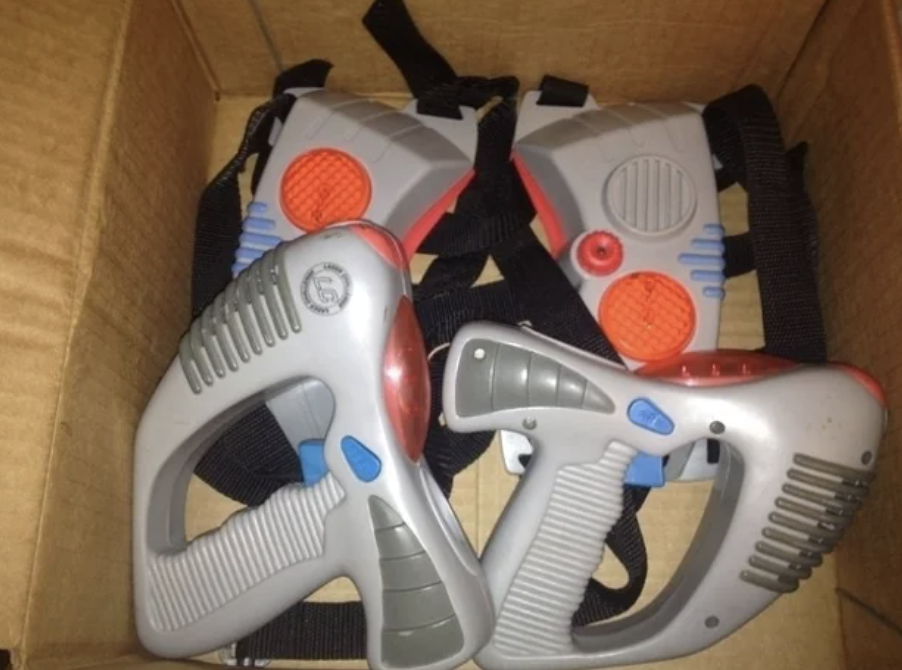 Box containing two gray toy laser guns with red and blue accents, alongside two matching vest targets with black straps.