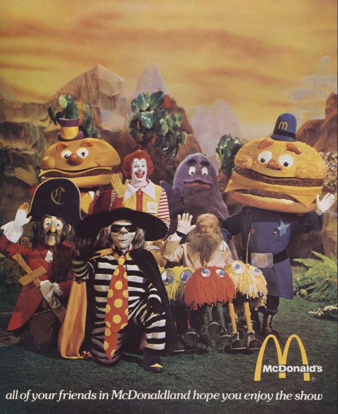 A group of McDonaldland characters stand together in colorful costumes. The characters include a clown, hamburgers, a purple blob, and others. A McDonald's logo is visible in the bottom right corner, with text reading, "all of your friends in McDonaldland hope you enjoy the show.