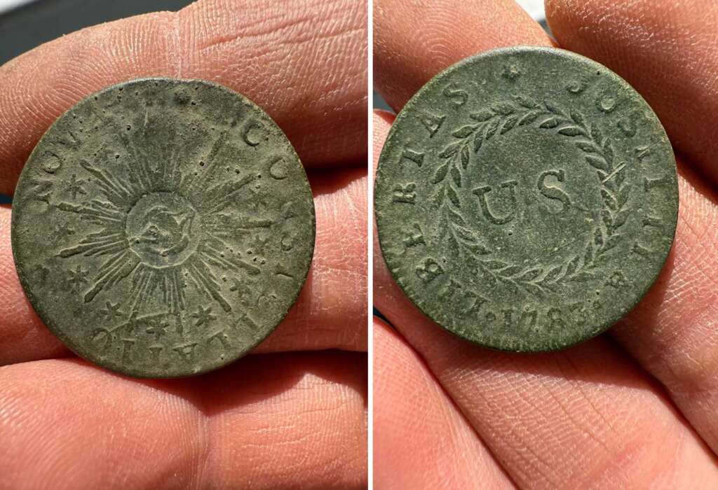 Close-up of a hand holding an old coin with two sides. One side shows a sunburst with an eye and the text "NOVA CONSTELLATIO." The other side features the letters "US" surrounded by a wreath and the date "1783 LIBERTAS JUSTITIA.